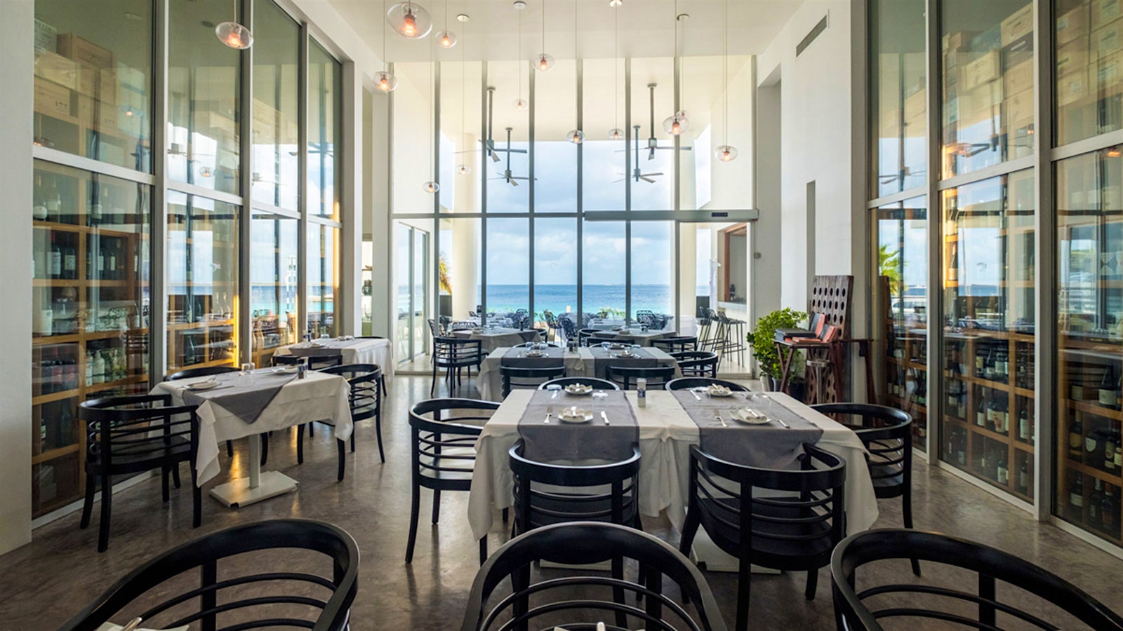 The white- and blue-colored, modern-design dining room at Capriccio Ristorante, with black wooden chairs and a view of the ocean